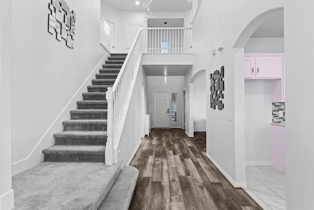 foyer entrance featuring baseboards, arched walkways, stairway, marble finish floor, and a high ceiling