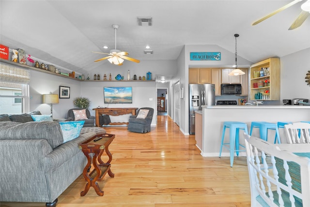 living area with a ceiling fan, visible vents, vaulted ceiling, and light wood-style flooring