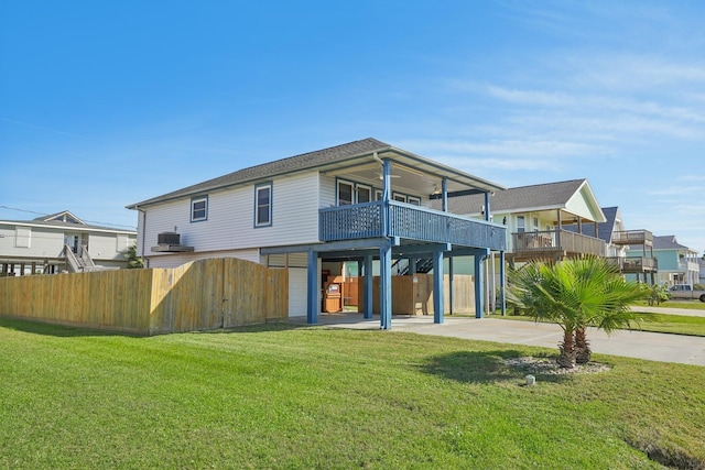 rear view of property with concrete driveway, a lawn, a balcony, and fence