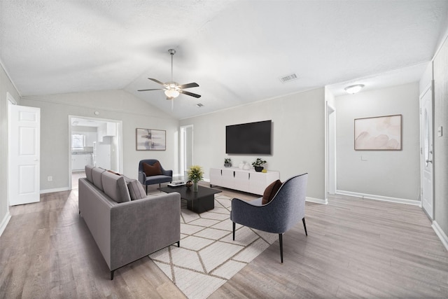 living area featuring lofted ceiling, visible vents, light wood-style flooring, a ceiling fan, and a textured ceiling