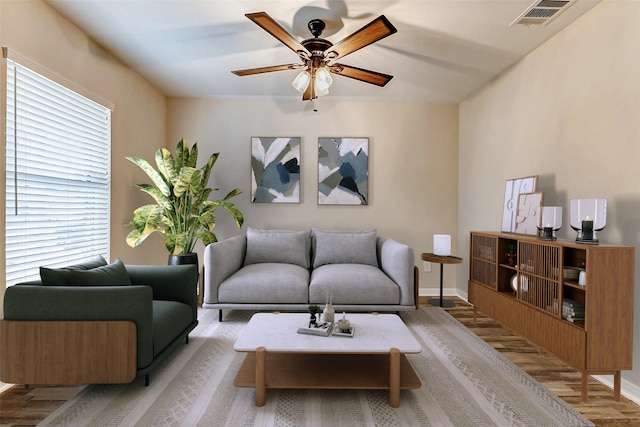 living area featuring a ceiling fan, wood finished floors, visible vents, and baseboards