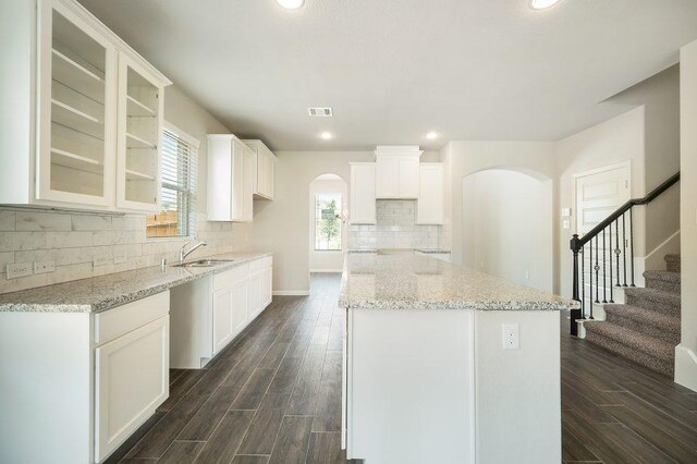 kitchen featuring arched walkways, a center island, white cabinetry, light stone countertops, and glass insert cabinets
