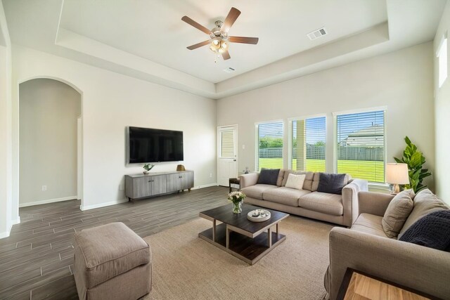 living area featuring dark wood finished floors, visible vents, a raised ceiling, and arched walkways
