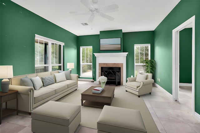 living area with visible vents, a tiled fireplace, a ceiling fan, and baseboards