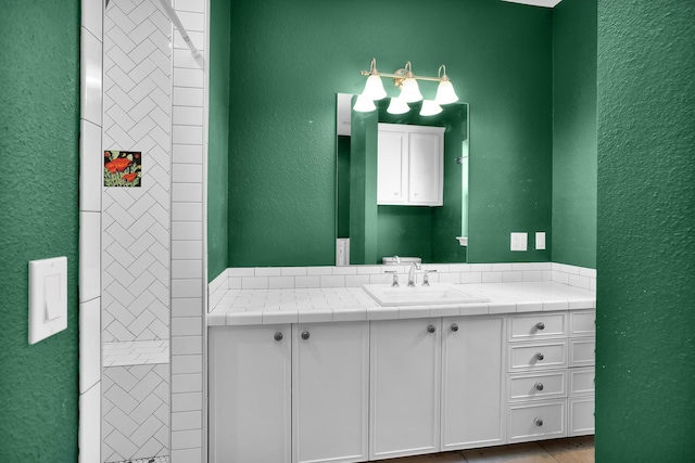 bathroom featuring a textured wall, tiled shower, and vanity