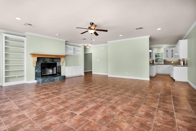 unfurnished living room featuring a high end fireplace, baseboards, visible vents, a ceiling fan, and crown molding