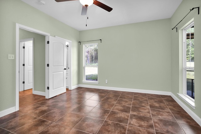 spare room with ceiling fan, dark tile patterned floors, and baseboards