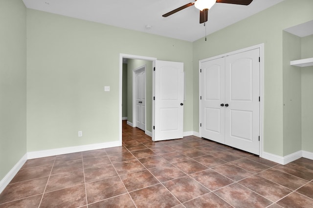 unfurnished bedroom with a ceiling fan, dark tile patterned flooring, a closet, and baseboards