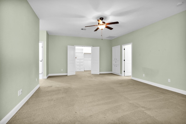 unfurnished bedroom featuring light carpet, baseboards, a walk in closet, and a ceiling fan