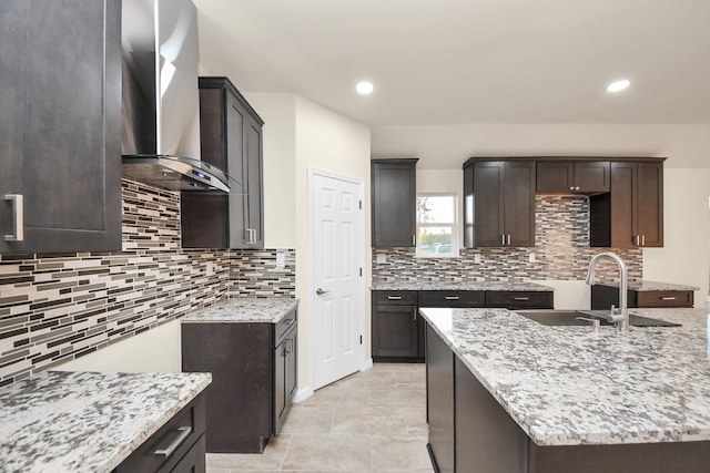 kitchen with wall chimney exhaust hood, light stone counters, and a sink