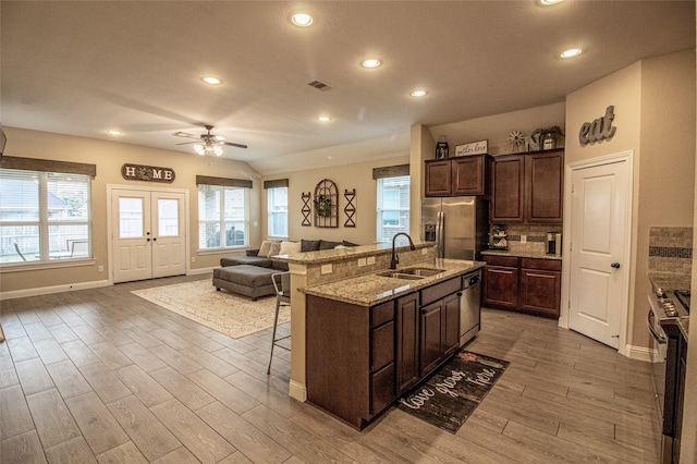 kitchen with a center island with sink, a kitchen breakfast bar, open floor plan, stainless steel appliances, and a sink