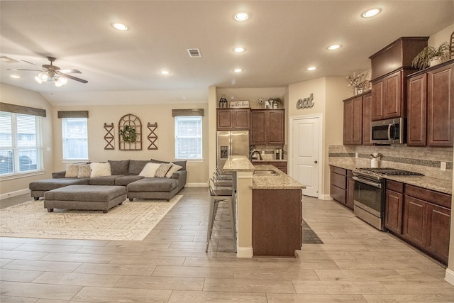 kitchen featuring stainless steel appliances, visible vents, open floor plan, a kitchen bar, and a center island with sink