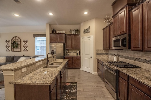 kitchen with dark brown cabinetry, backsplash, a kitchen island with sink, stainless steel appliances, and a sink