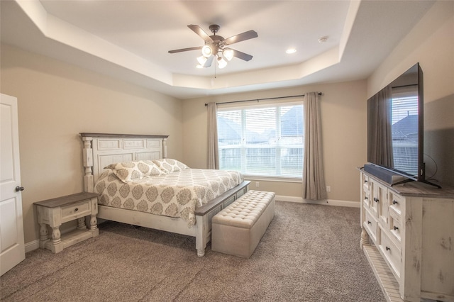 carpeted bedroom featuring ceiling fan, a raised ceiling, and baseboards