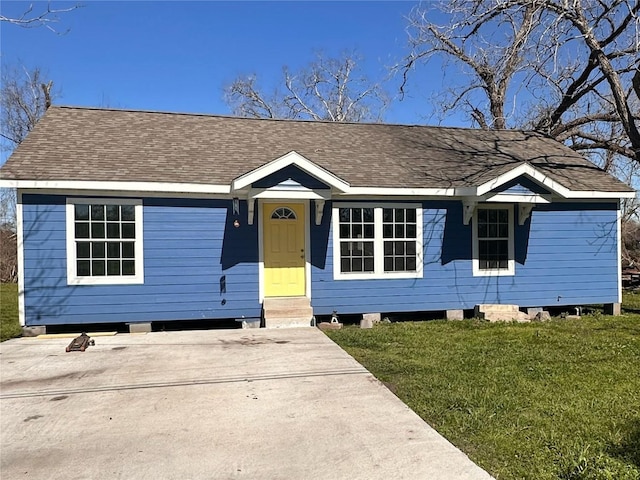 ranch-style house featuring entry steps, driveway, a front lawn, and roof with shingles