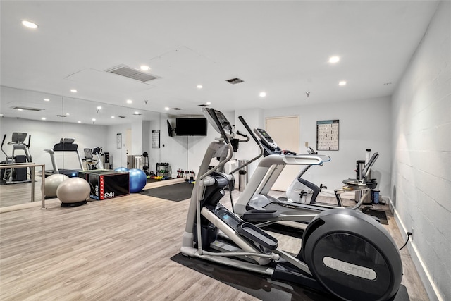 gym featuring concrete block wall, light wood-style flooring, visible vents, and recessed lighting