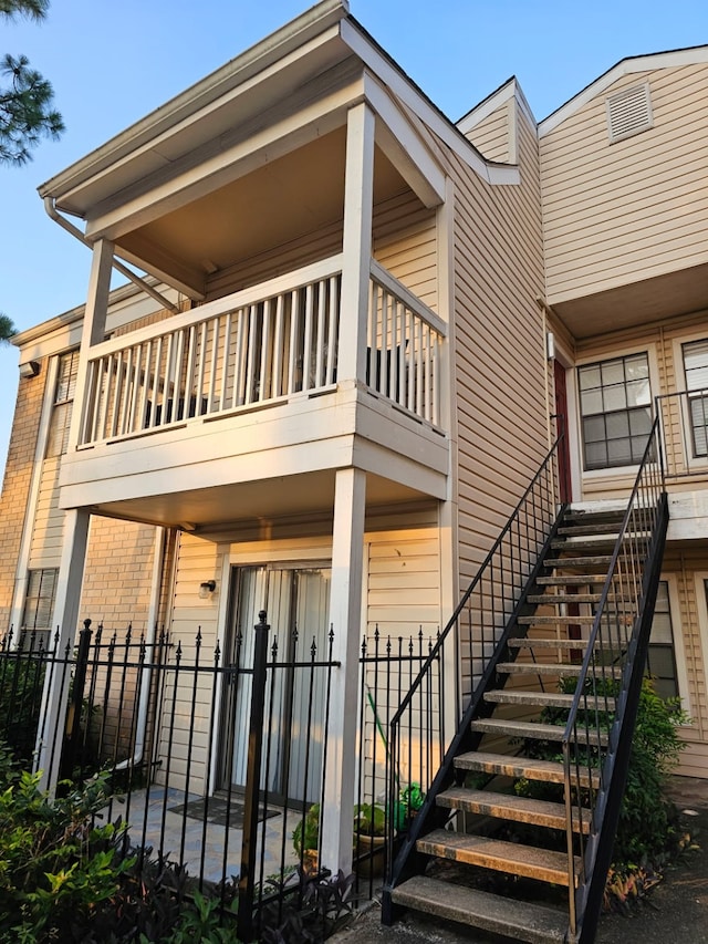 exterior space with a balcony, stairs, fence, and brick siding