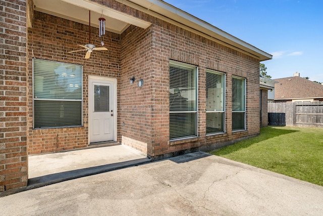 entrance to property with ceiling fan, fence, a yard, a patio area, and brick siding