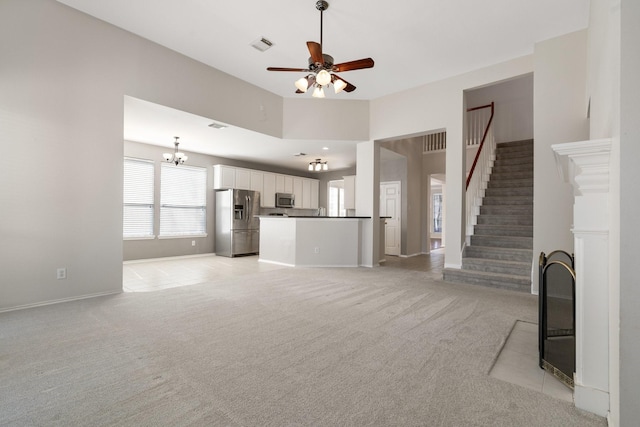 unfurnished living room with light colored carpet, ceiling fan with notable chandelier, a high ceiling, visible vents, and stairway