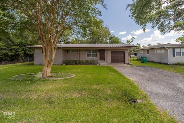 ranch-style home featuring a garage, driveway, metal roof, and a front yard