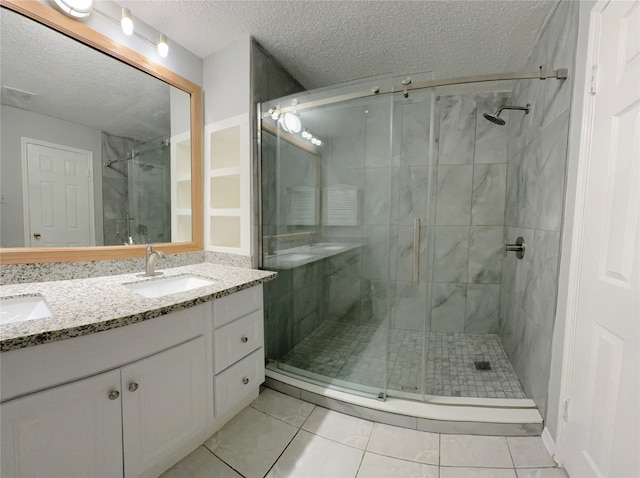 full bathroom featuring a textured ceiling, a sink, a shower stall, tile patterned floors, and double vanity