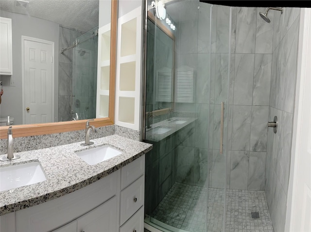 bathroom with a textured ceiling, double vanity, a sink, and a shower stall