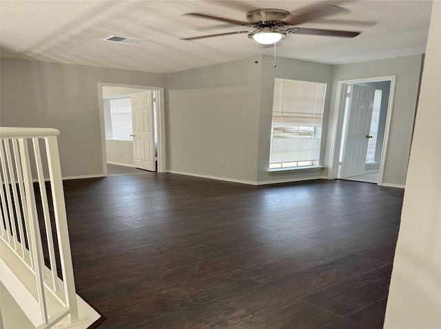 unfurnished room featuring a textured ceiling, a ceiling fan, visible vents, baseboards, and dark wood-style floors