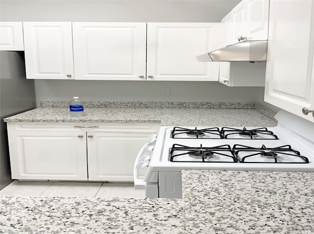 kitchen featuring white gas range oven, white cabinets, freestanding refrigerator, light stone countertops, and under cabinet range hood