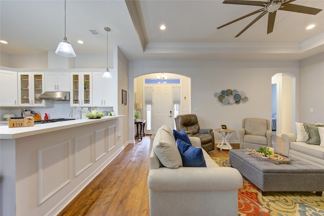 living room featuring arched walkways, a tray ceiling, and wood finished floors