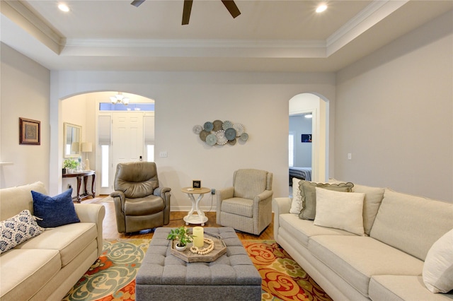 living room with light wood-style floors, arched walkways, a raised ceiling, and ornamental molding