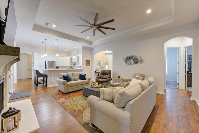 living room featuring arched walkways, crown molding, a raised ceiling, visible vents, and light wood-style floors