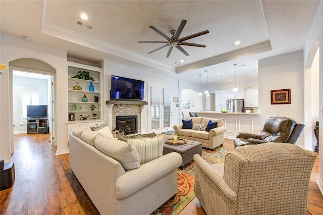 living room featuring arched walkways, a raised ceiling, and dark wood-style flooring