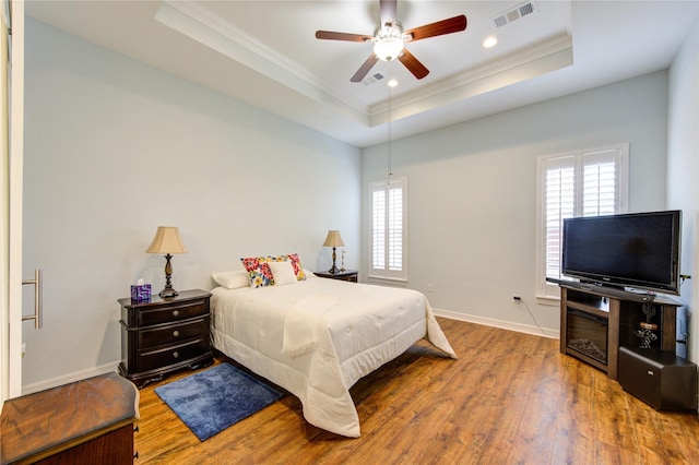 bedroom with visible vents, multiple windows, a tray ceiling, and wood finished floors