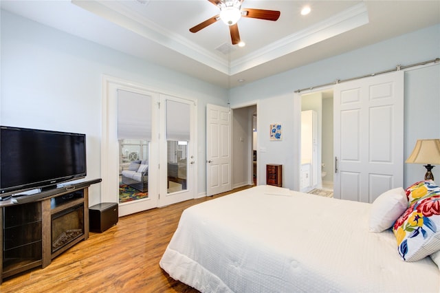 bedroom featuring a barn door, light wood-type flooring, a raised ceiling, and crown molding