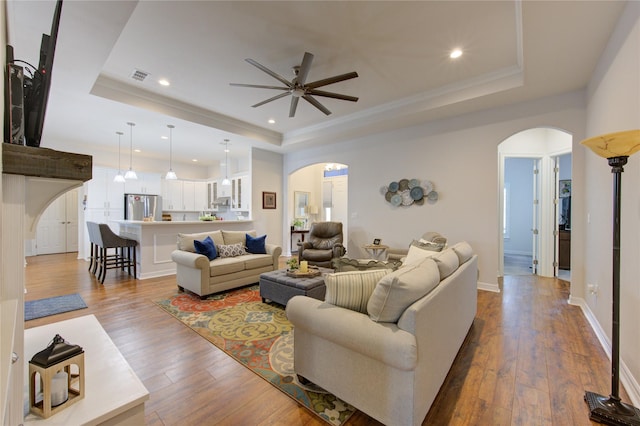 living area with arched walkways, a raised ceiling, visible vents, and light wood finished floors