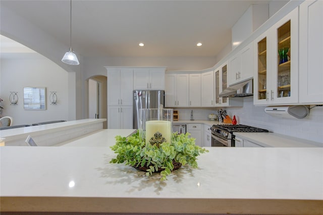 kitchen with under cabinet range hood, stainless steel appliances, white cabinetry, light countertops, and glass insert cabinets