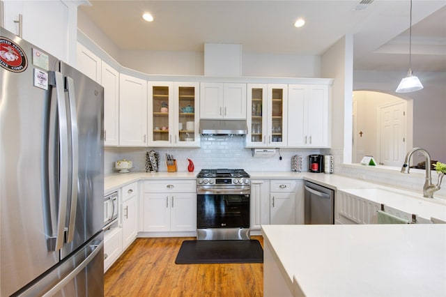 kitchen featuring stainless steel appliances, light countertops, glass insert cabinets, a sink, and exhaust hood