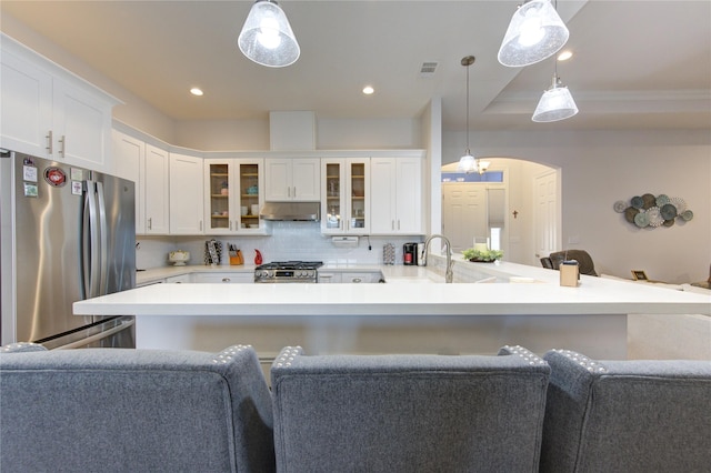 kitchen featuring arched walkways, glass insert cabinets, appliances with stainless steel finishes, light countertops, and pendant lighting