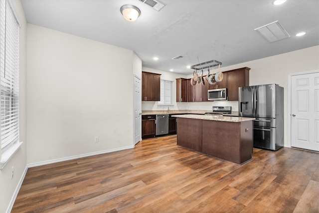 kitchen featuring stainless steel appliances, a wealth of natural light, a kitchen island, and dark brown cabinetry