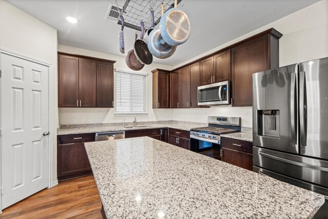 kitchen featuring dark brown cabinetry, light wood finished floors, light stone counters, and stainless steel appliances