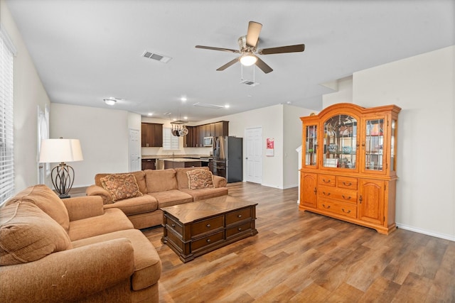 living room featuring ceiling fan, wood finished floors, visible vents, and baseboards