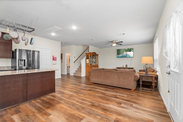 living room with a ceiling fan, visible vents, stairway, and wood finished floors