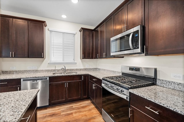 kitchen with dark brown cabinetry, light wood finished floors, appliances with stainless steel finishes, light stone counters, and a sink