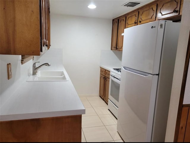 kitchen featuring white appliances, a sink, visible vents, light countertops, and brown cabinets