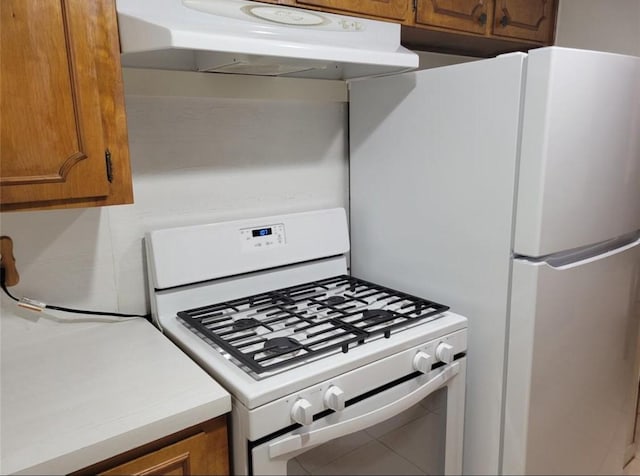 kitchen with brown cabinetry, white appliances, light countertops, and under cabinet range hood