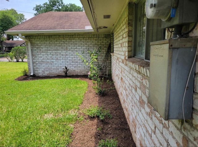 exterior space featuring brick siding, a lawn, and roof with shingles