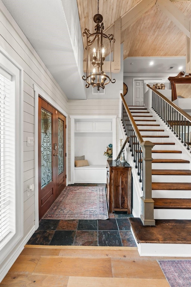 foyer with stairway, stone tile floors, a chandelier, and wood walls