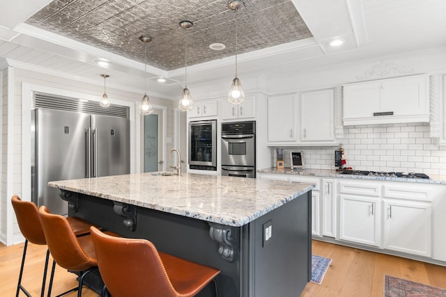 kitchen featuring stainless steel appliances, a tray ceiling, white cabinetry, and an island with sink