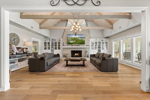 living area with visible vents, light wood-style flooring, beamed ceiling, an inviting chandelier, and a stone fireplace