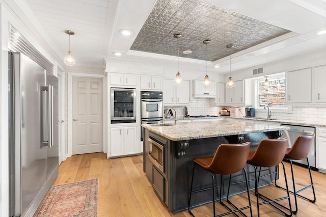 kitchen with pendant lighting, white cabinetry, an island with sink, and built in appliances